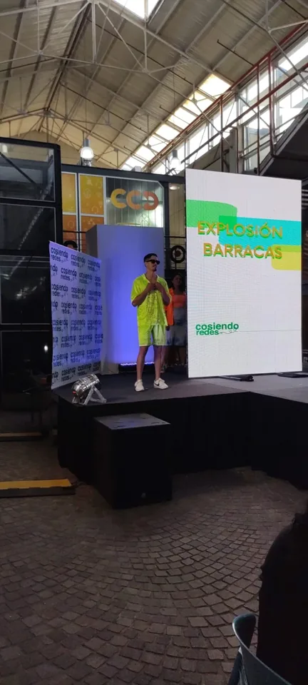Una participante presenta su prenda junto a la pantalla del evento.
